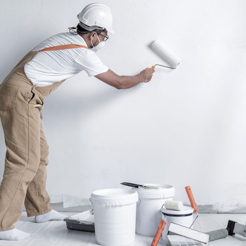 man-paints-white-wall-with-roller-repair-interior